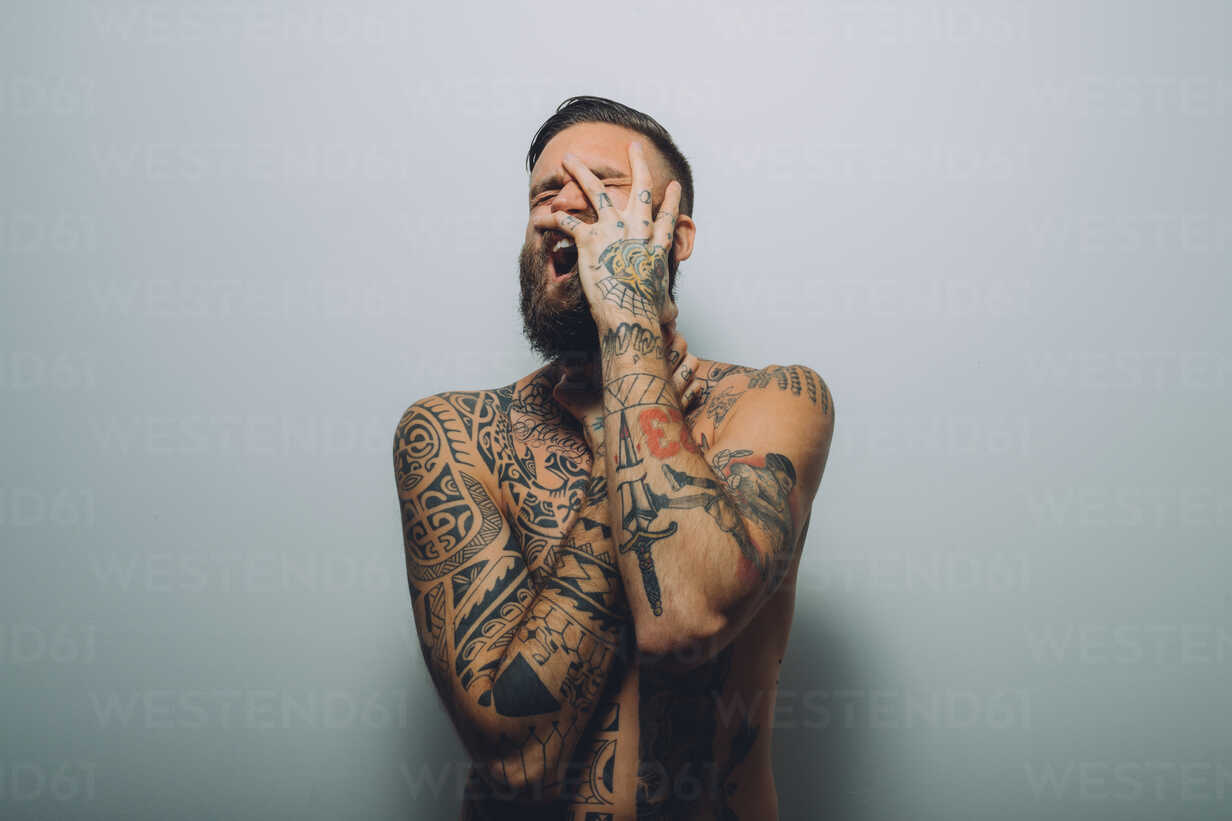 Portrait of young man with beard, covered in tattoos, hand on face,  screaming stock photo