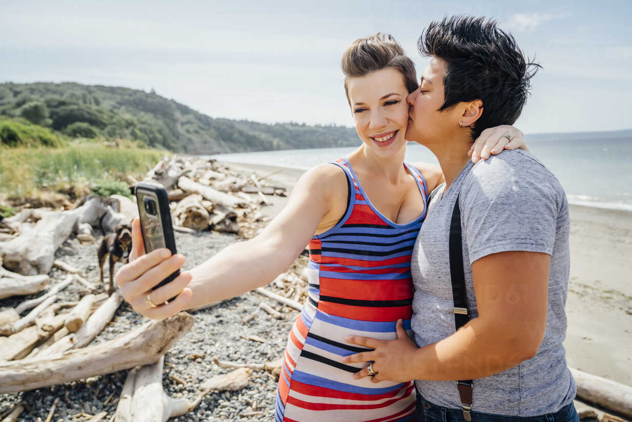 Pregnant lesbian couple posing for cell phone selfie on beach ...