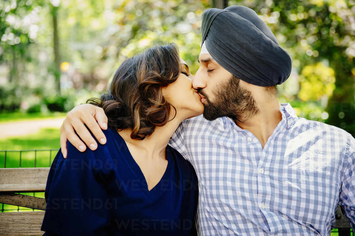 Indian couple kissing on bench in urban park stock photo