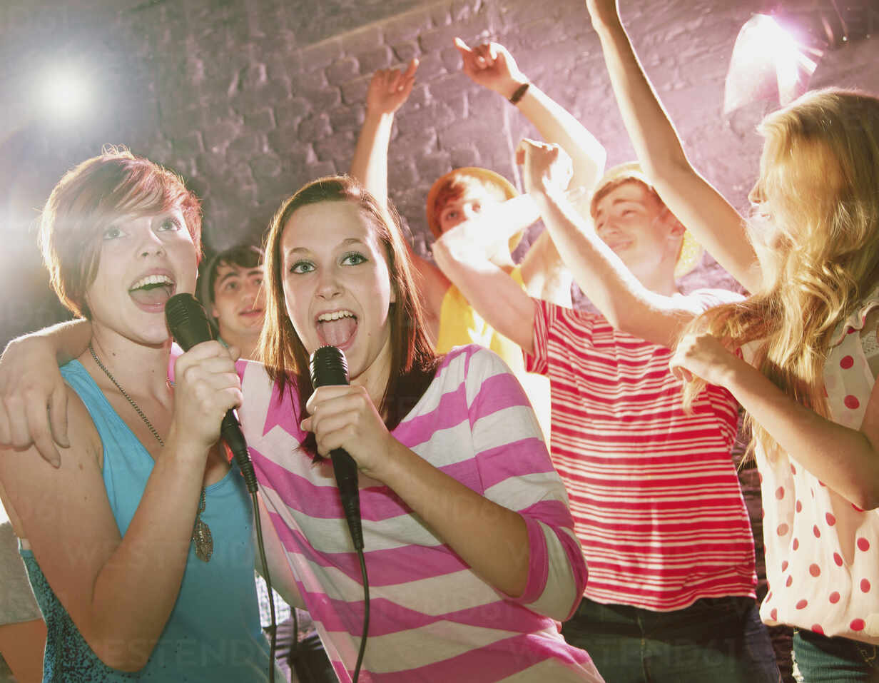 Happy teenage friends singing karaoke at party stock photo