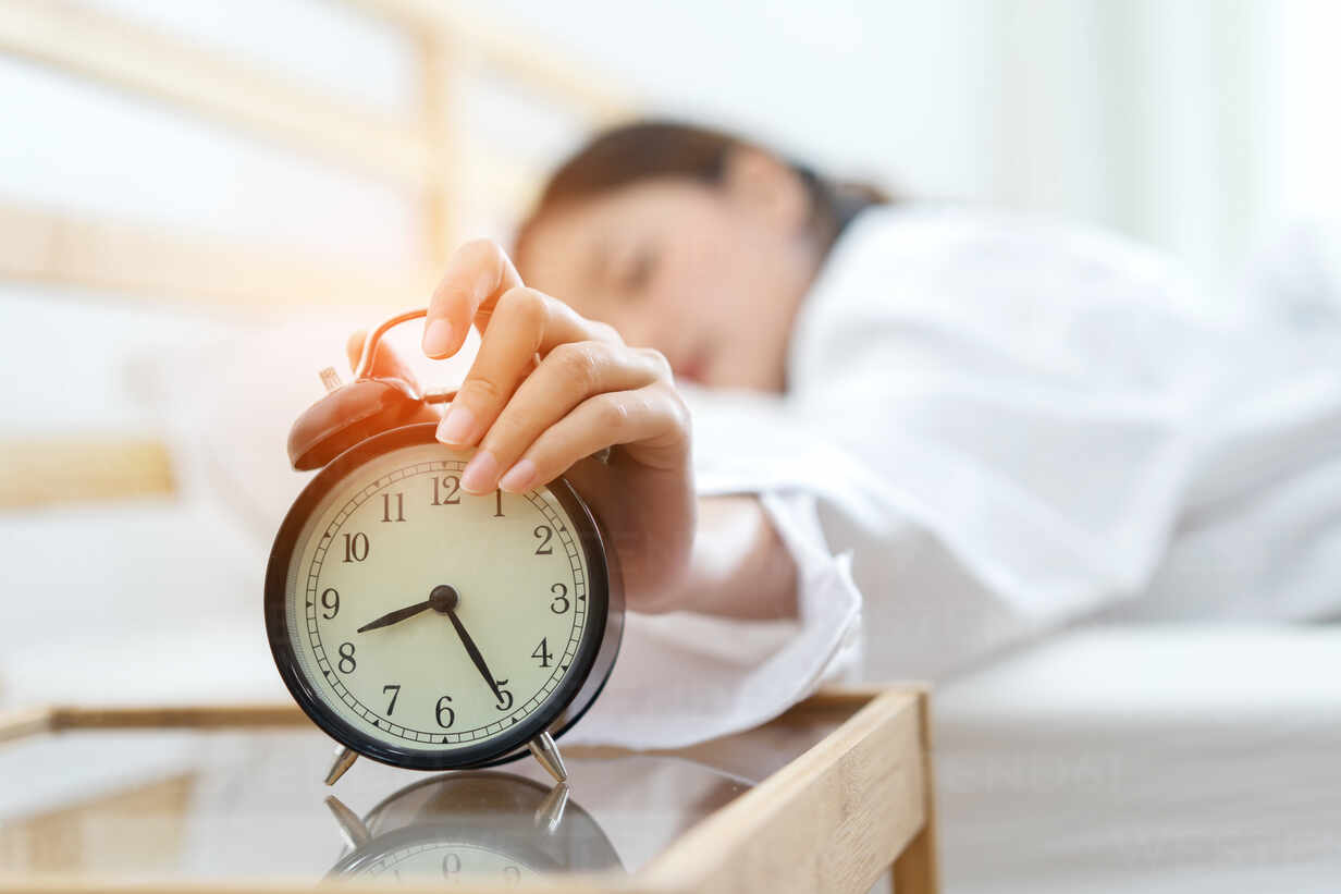 Woman Snoozing Alarm Clock While Sleeping On Bed At Home stock photo