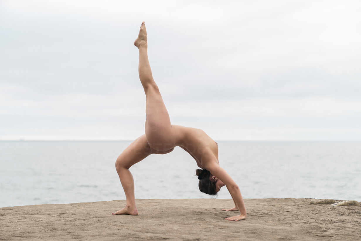 Flexible young naked woman practicing bending over backwards