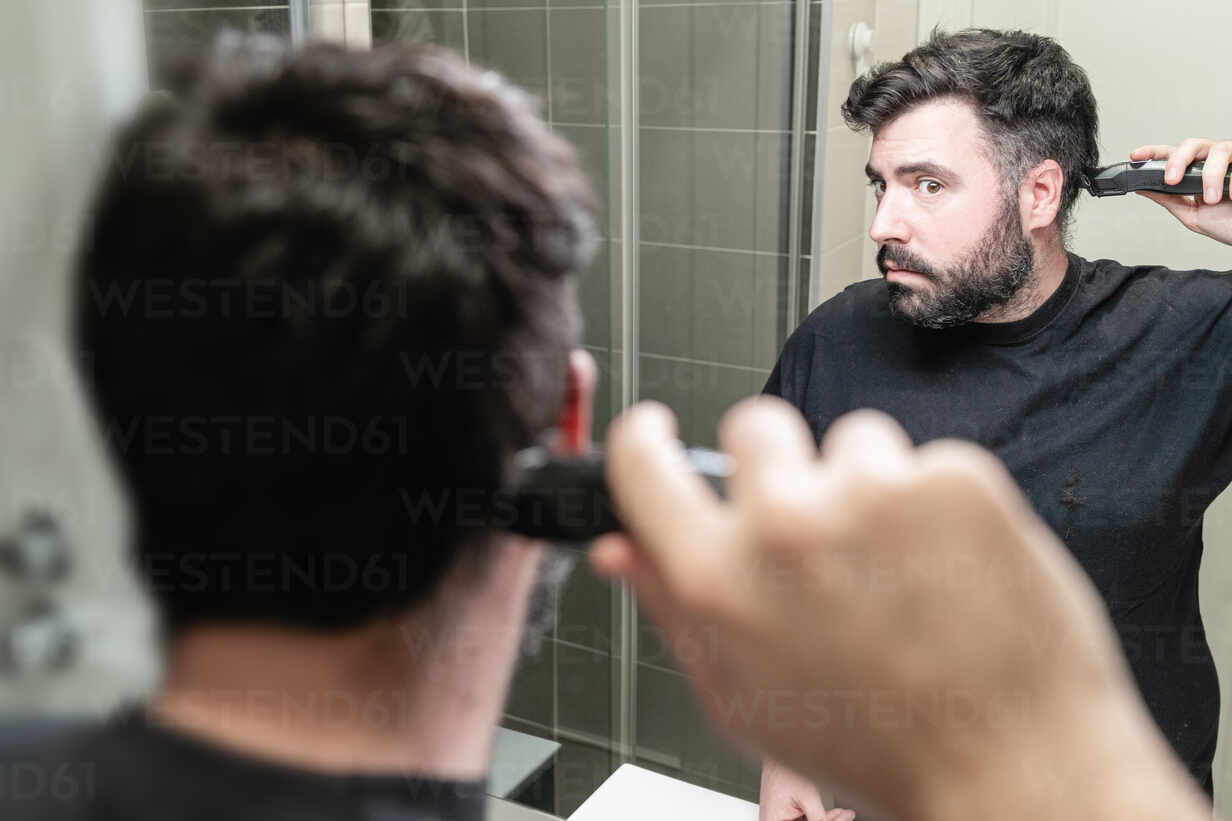 Self haircut. A man is cutting his hair with a hair clipper in the bathroom  stock