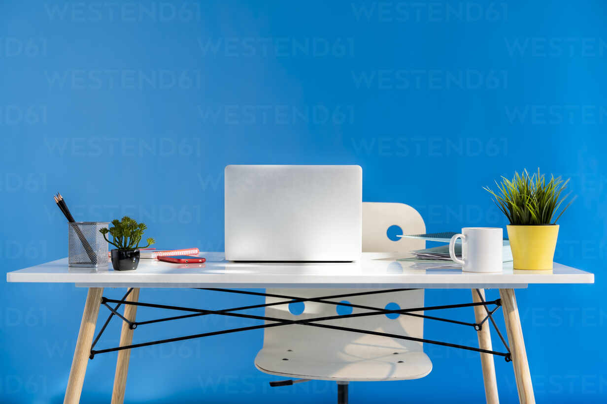 Office desk with laptop and blue wall in the background stock photo