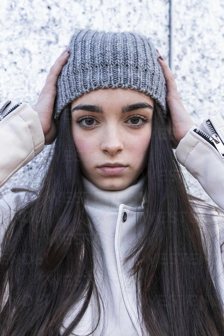Teenage girl in knit hat with long hair against wall stock photo