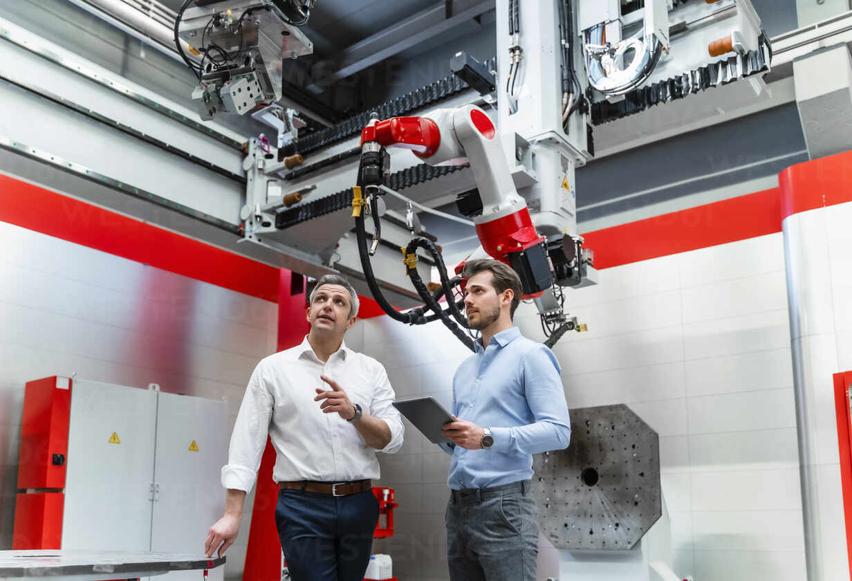 Mature automation engineer explaining robotic to young man with digital tablet in factory stock photo