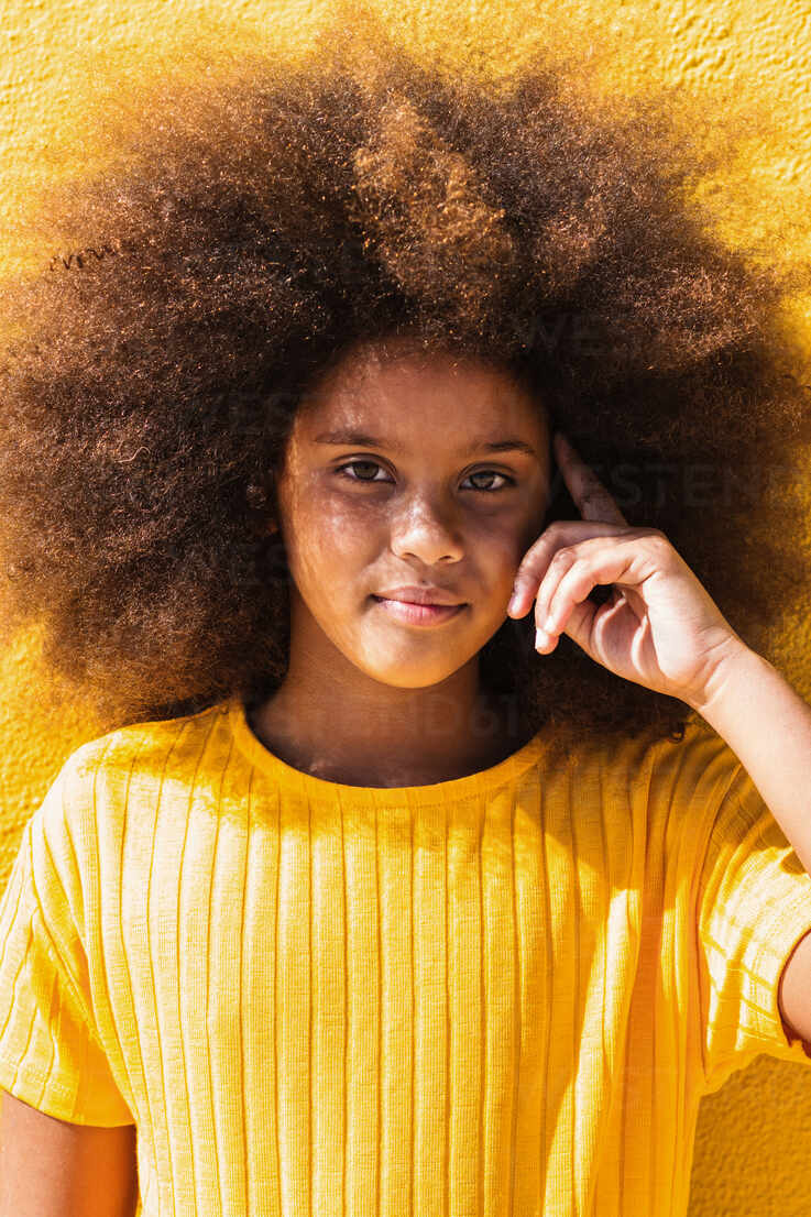 Teen African American girl with fluffy curly hair wearing yellow sweatshirt  touching temple and looking at