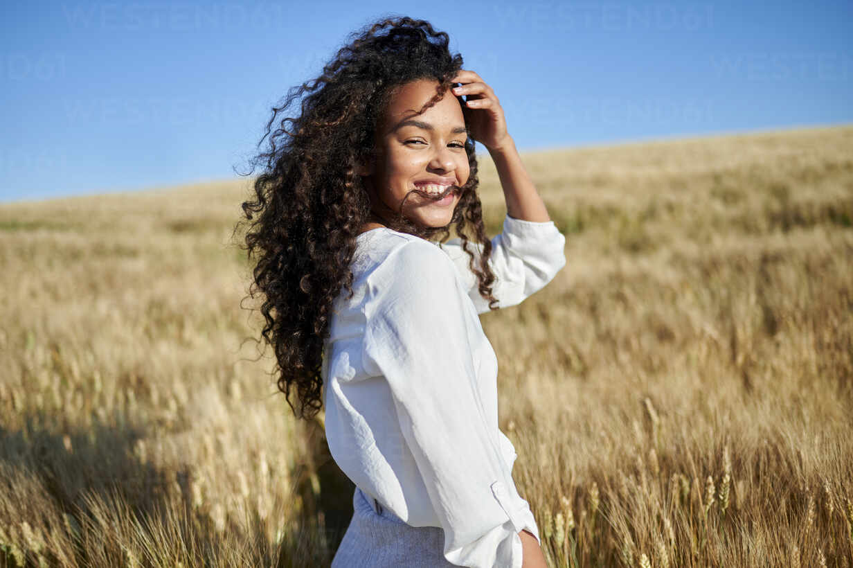 Beautiful young curly haired woman with hand in hair at wheat field stock  photo