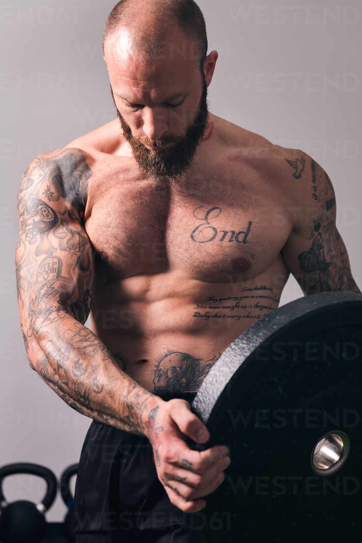 Sportsman with muscular body and naked torso standing with heavy weight  plate in gym stock photo