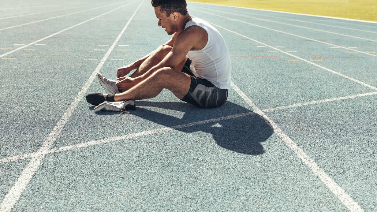 Athlete sitting on a running track tying shoe lace. Runner sitting on ...